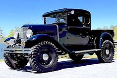 an old black truck is parked on the side of the road next to some water