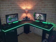 a computer desk with two monitors and a keyboard on it in front of a brick wall