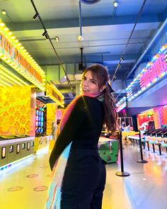 a woman is standing in front of some arcade machines with neon lights on the ceiling