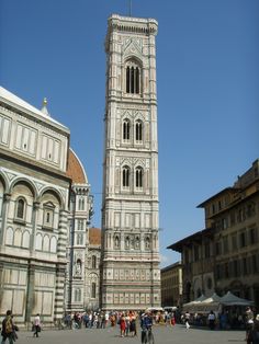 a tall clock tower towering over a city filled with buildings and people walking around it