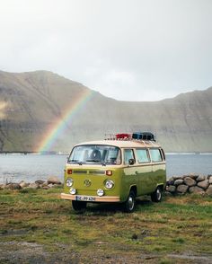 an old vw camper van parked in front of a lake with a rainbow