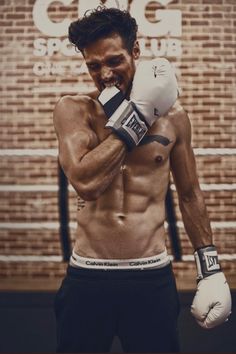 a shirtless man wearing boxing gloves and holding a punching glove in front of a brick wall