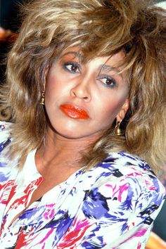 a close up of a person with long hair and orange lipstick on her face, wearing a floral shirt