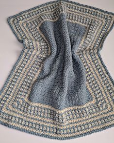 a crocheted blanket is laying on top of a white table with blue and yellow squares