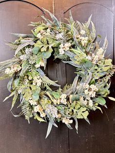 a wreath is hanging on a door with greenery and white flowers in the center