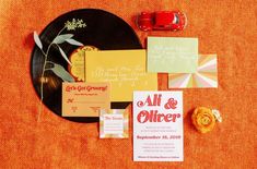 the wedding stationery is laid out on an orange table cloth with a red car