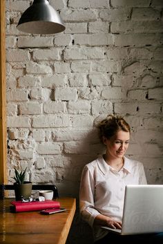 a woman sitting in front of a laptop computer on top of a wooden desk next to a lamp