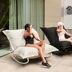 two women sitting on lounge chairs in front of a glass door, one with her hand up to her head