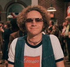 a man with curly hair and glasses standing in front of a group of other people