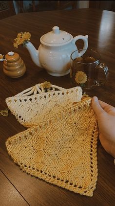 a person is crocheting on a table with some teapots and other items