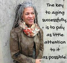 a woman with dreadlocks standing in front of a wall that says, the key to aging successfully is to pay as little attention to it as possible