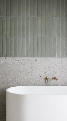 a white bath tub sitting next to a wall with tile on it's sides