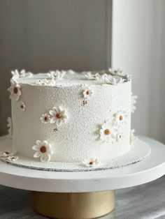 a white cake with flowers on it sitting on top of a table in front of a window