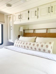 a bed with white sheets and pillows in a bedroom next to a window that looks out onto the ocean