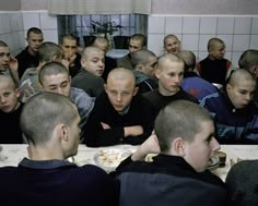 a large group of men sitting at a table eating pizza and drinking beer in a room with white tiles on the walls