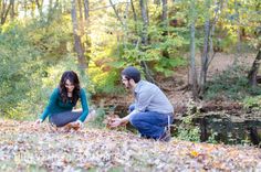 a man kneeling down next to a woman on top of a leaf covered hillside in the woods