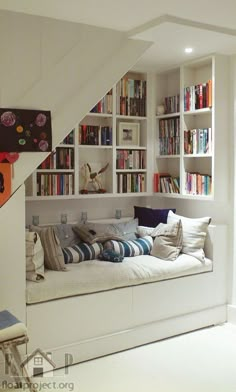 a living room filled with lots of furniture and bookshelves next to a stair case