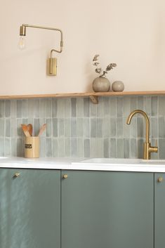 a kitchen with green cabinets and gold faucets on the counter top, next to a white sink