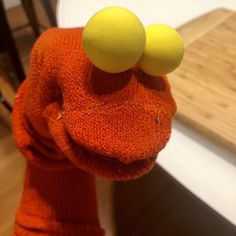 an orange stuffed animal with two yellow balls on it's head, sitting in front of a table