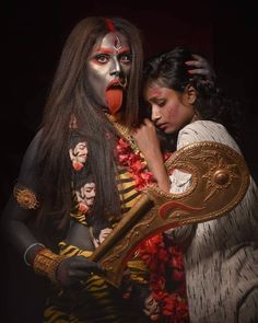 two women dressed in costumes and makeup holding a large mirror