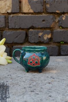 a green mug sitting on top of a cement surface next to flowers and a brick wall