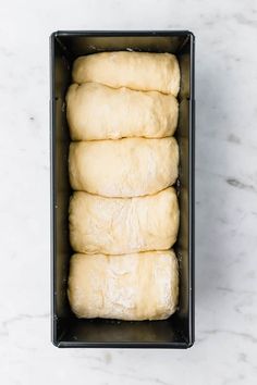 four uncooked dough rolls in a black box on a white marble countertop