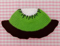 a crocheted green and brown hat sitting on top of a pink checkered table cloth