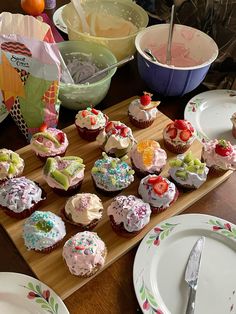 cupcakes are arranged on a wooden tray with plates and bowls in the background