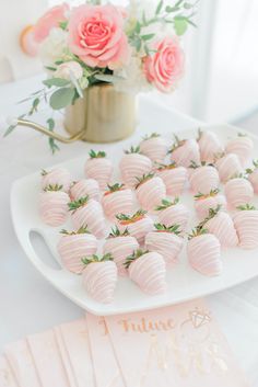 strawberries are arranged on a white platter with pink flowers