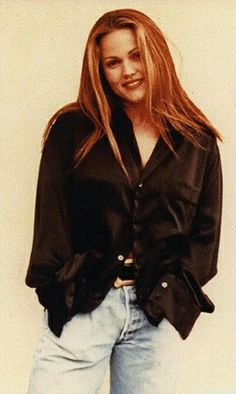 a woman with long blonde hair wearing a black shirt and jeans, posing for the camera