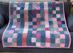 a blue couch with a patchwork quilt on it's back and pink trim around the edges