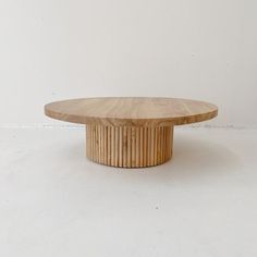 a round wooden table sitting on top of a white floor next to a black cat