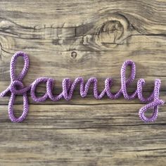 the word family written in crochet on a wooden background with purple yarns