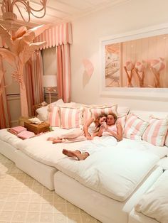 two people laying on a large white couch in a room with pink and white decor