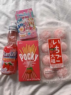 japanese snacks and drinks on a bed with white sheets in the foreground, along with an unopened bottle of ramune strawberry milk