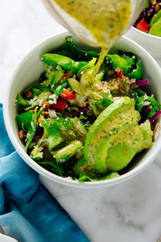 a bowl filled with salad and dressing being drizzled on top of it