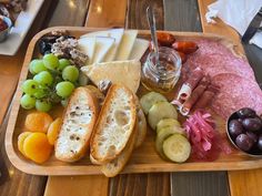 a wooden tray topped with lots of different types of cheese and meats next to fruit