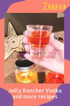 a hand holding a glass filled with liquid next to two jars and a star on the table