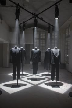 three suits are on display in an empty room with light coming through the windows and casting shadows