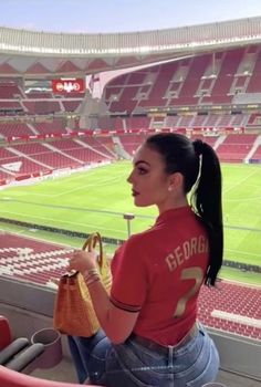 a woman sitting in the bleachers at a stadium holding a purse and looking out