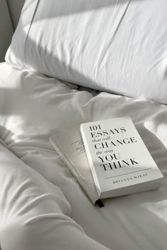 a book sitting on top of a white bed next to pillows and pillowcases