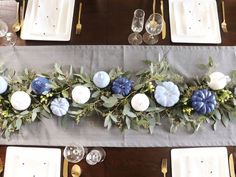 the table is set with blue and white flowers, greenery and candles on it