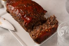 meatloaf on a white plate with knife and glass of water in the background