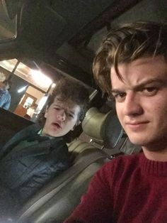 two young men are sitting in the back seat of a car and one is looking at the camera