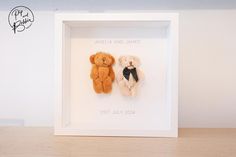 two teddy bears in a white frame on a wooden table next to a wall with the name amelia and james