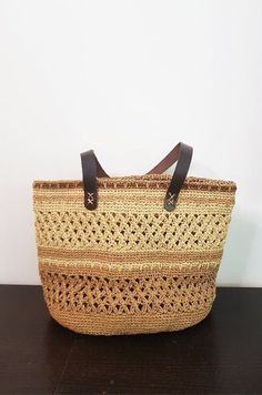 a straw bag sitting on top of a wooden table next to a white wall and black leather handles