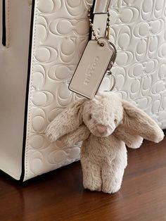 a small stuffed animal sitting next to a white handbag on a wooden floor in front of a purse