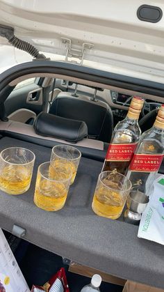 three bottles of alcohol are sitting in the trunk of a car with glasses on it