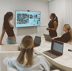 three women are sitting at a table with laptops in front of them and one woman is pointing to the screen