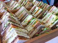 many sandwiches are stacked on top of each other in wooden trays at a buffet table